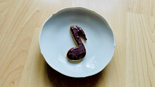 Foto eines mit dunkler Schokolade überzogenen Plätzchens in Form einer Achtelnote: A SHORT NOTE zum Tag der Zartbitter-Schokolade